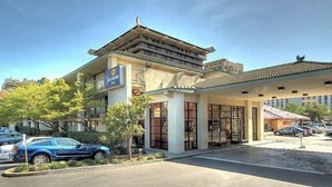 A hotel with a traditional architectural style, a covered entrance, and a parking lot with cars.
