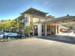 A hotel with a traditional architectural style, a covered entrance, and a parking lot with cars.