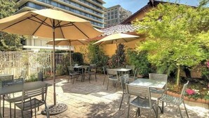 An outdoor patio with tables and chairs, surrounded by a fence and greenery.