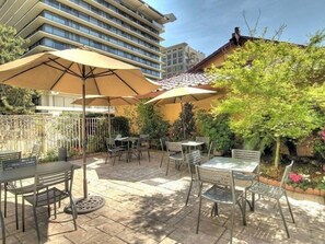 An outdoor patio with tables and chairs, surrounded by a fence and greenery.