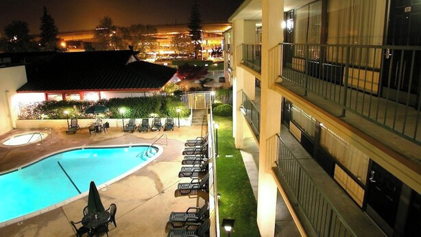 A hotel pool area with a swimming pool, lounge chairs, and a building with balconies.