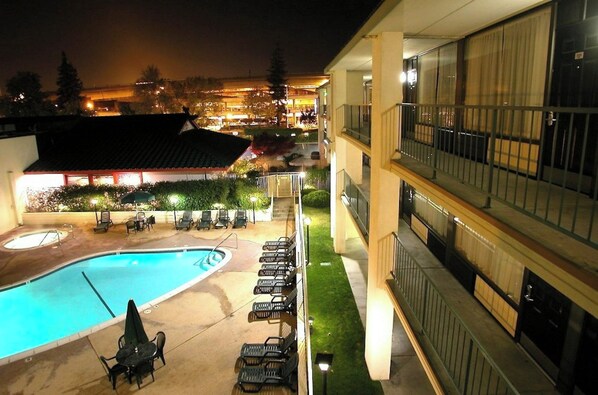 A hotel pool area with a swimming pool, lounge chairs, and a building with balconies.