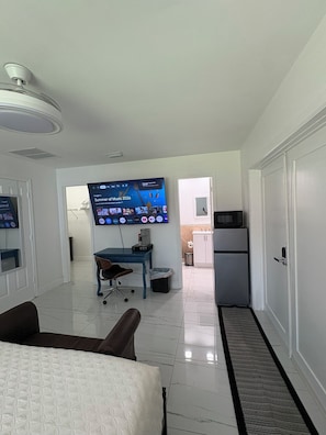 A hotel room with a bed, a desk with a computer, a TV mounted on the wall, and a kitchenette. - Large studio in Wellington (Wellington)