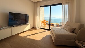 A modern living room with a flat-screen TV, a sofa, and a balcony with a view of the sea. - Sea View & Pool, Elite Resort (Saranda)