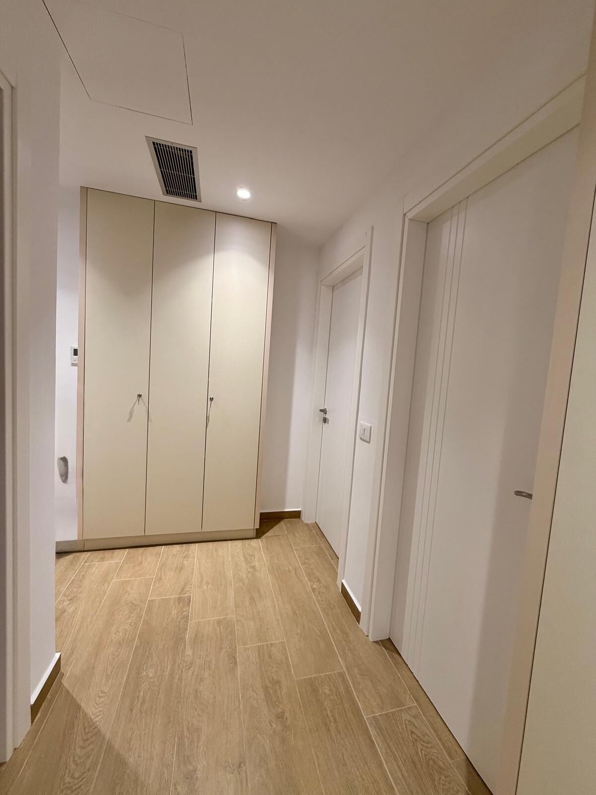 Un corridoio con un armadio, una porta e una griglia di ventilazione a soffitto.