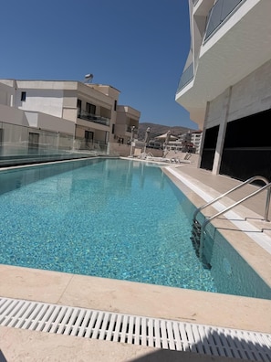 Una piscina con agua cristalina, rodeada por una zona de piscina con sillones de playa y sombrillas.