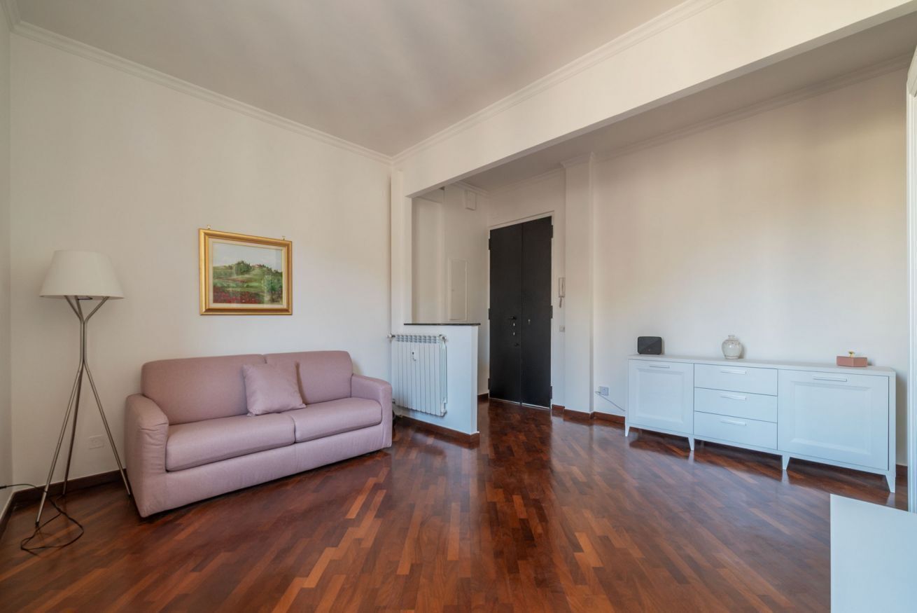 A spacious room with a wooden floor, a pink sofa, a radiator, a white cabinet, and a framed picture on the wall.