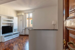 Una stanza con pavimento in legno, mobili bianchi, una TV a schermo piatto e una finestra con persiane.