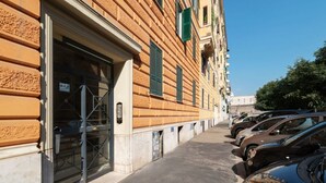 A row of parked cars along a sidewalk adjacent to a building with a large open door and a window with green shutters. - An elegant 75 sqm apartment, ideal for 4 people, located on the 6th and top floor of a building with an elevator (NOT accessible to people with disabilities).The Lodi metro station is just a 4-minute walk away, making it easy to get around the capital. (Rome)