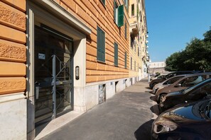A row of parked cars along a sidewalk adjacent to a building with a large open door and a window with green shutters. - An elegant 75 sqm apartment, ideal for 4 people, located on the 6th and top floor of a building with an elevator (NOT accessible to people with disabilities).The Lodi metro station is just a 4-minute walk away, making it easy to get around the capital. (Rome)