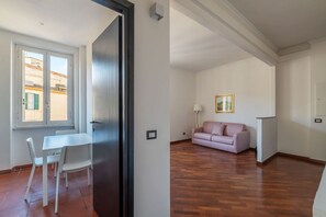 A room with a wooden floor, a white table with chairs, a pink sofa, and a framed picture on the wall. - An elegant 75 sqm apartment, ideal for 4 people, located on the 6th and top floor of a building with an elevator (NOT accessible to people with disabilities).The Lodi metro station is just a 4-minute walk away, making it easy to get around the capital. (Rome)