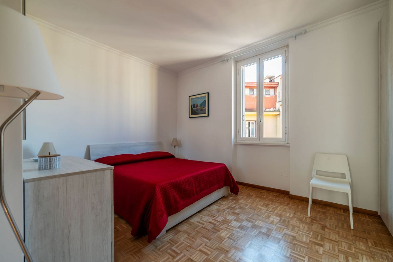 Ein Schlafzimmer mit Bett, Stuhl, Schreibtisch, Fenster und einem Bild an der Wand.