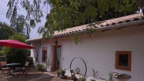 A white building with a tiled roof, a red umbrella, and potted plants.
