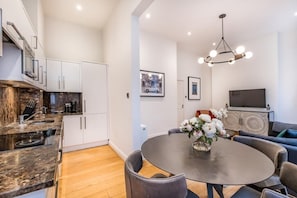 Una cocina moderna con armarios blancos, una mesa de comedor con sillas y una sala de estar con sofá y televisor.