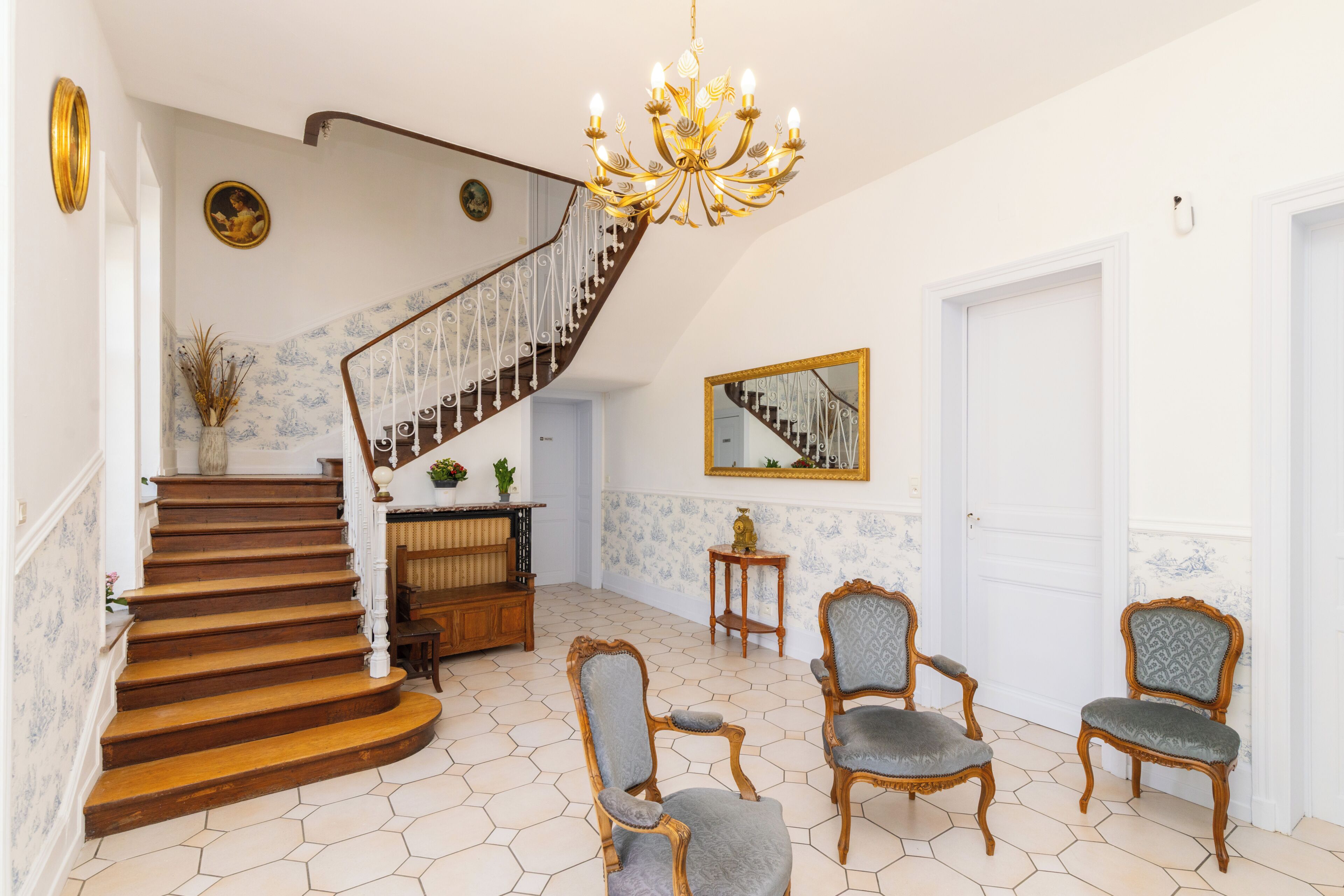Eine prächtige Treppe mit einem Chandelier, verzierten Stühlen und einem Spiegel an der Wand.