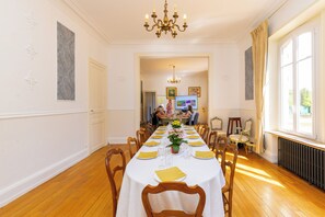 A dining room with a long table set for a meal, wooden chairs, a chandelier, and a view of a garden through the window. - Le Domaine d'Amélie: An Elegant Vacation Rental on the Outskirts of Nancy (Dombasle-sur-Meurthe)