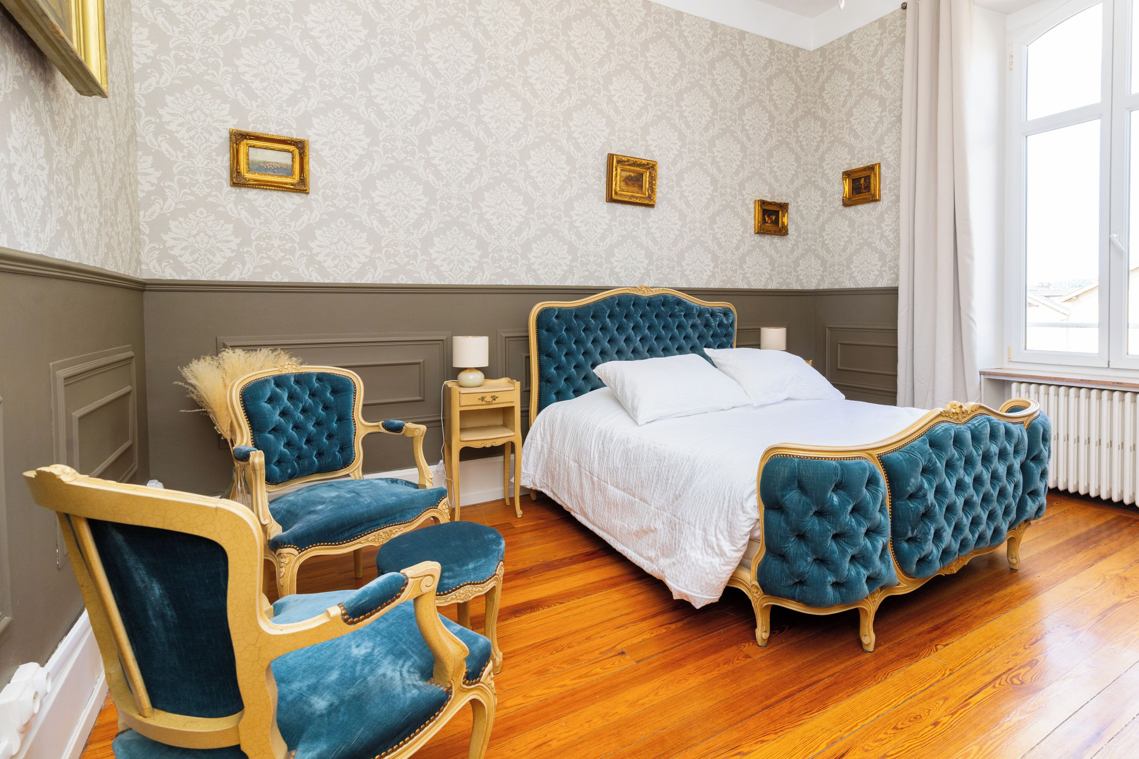 Een slaapkamer met een groot bed, twee fauteuils, een nachtkastje en drie ingelijste foto's aan de muur.
