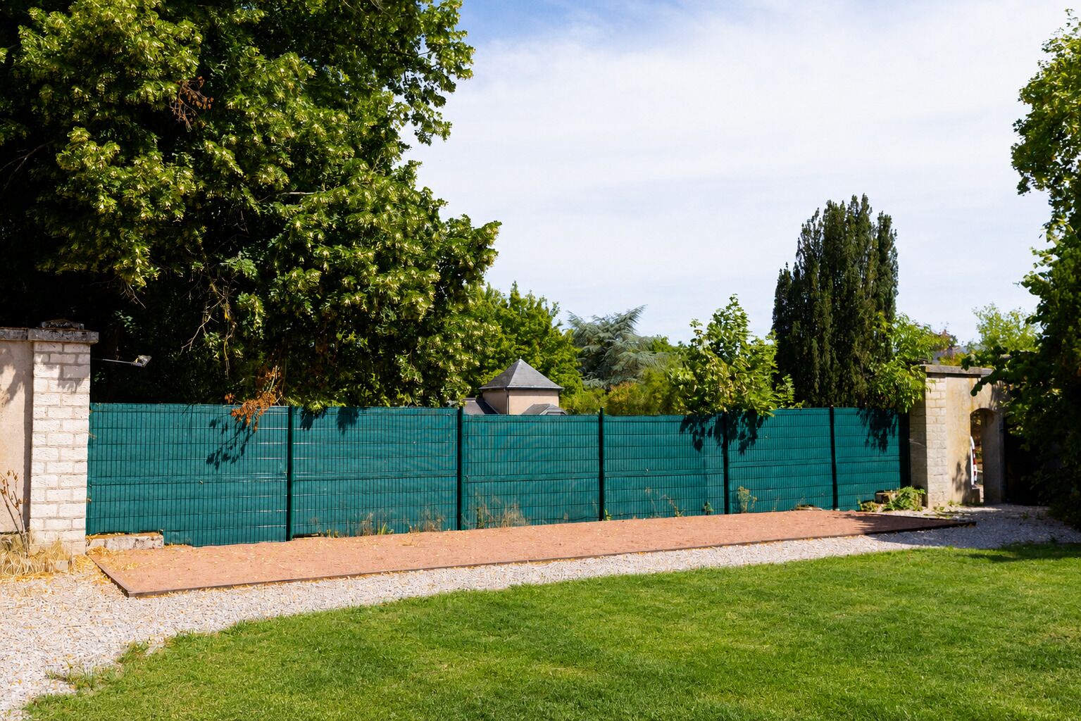 A fenced backyard with a grassy lawn, a brick pathway, and a stone wall.
