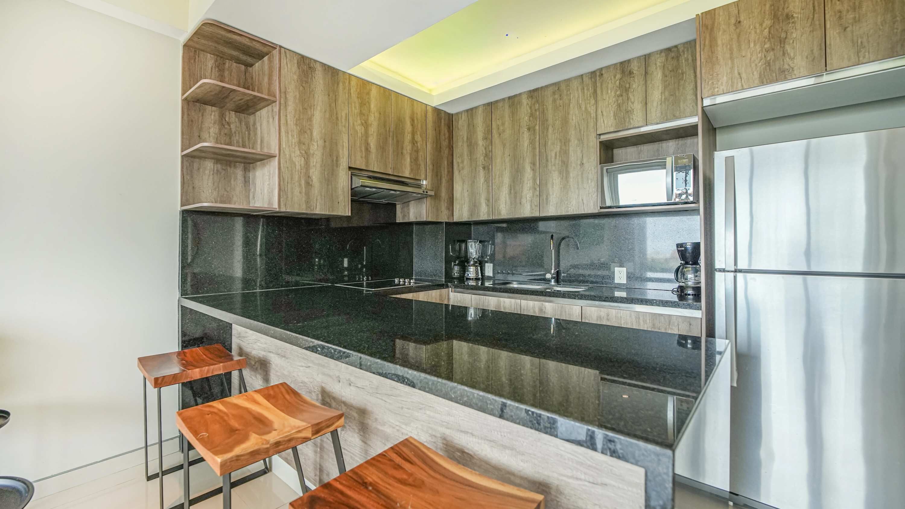 Eine moderne Küche mit schwarzer Arbeitsplatte, Edelstahlgeräten, Holzschränken und einer Bar mit Barhocker.