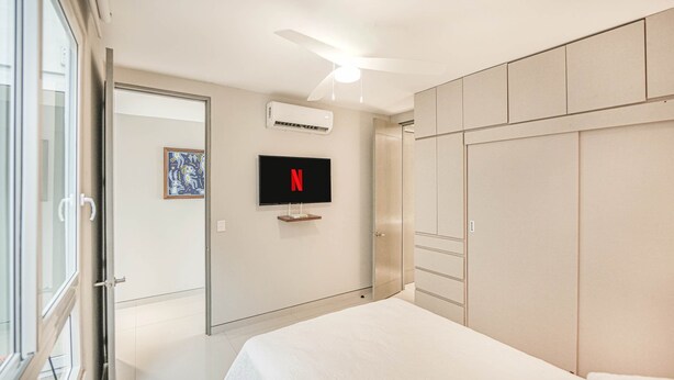 Ein modernes Schlafzimmer mit Bett, Kleiderschrank, Deckenventilator, Klimaanlage und einem an der Wand montierten Fernseher.
