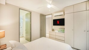 Ein Hotelzimmer mit einem Bett, einem an der Wand befestigten Fernseher, einem Kleiderschrank und einem Deckenventilator.