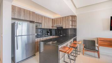 A modern kitchen with a stainless steel refrigerator, black countertops, wooden cabinets, and a bar area with stools.
