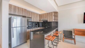Eine moderne Küche mit Edelstahlkühlschrank, schwarzen Arbeitsplatten, Holzschränken und einer Bar mit Hockern.