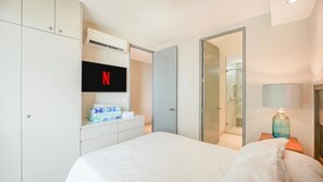 Een hotelkamer met een bed, een aan de muur bevestigde televisie, een kledingkast, een badkamer met douche en een nachtkastje met lamp.