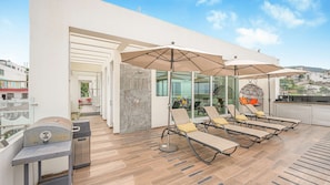 Eine Dachterrasse mit Liegestühlen, einem Grill und Sitzgelegenheiten im Freien.