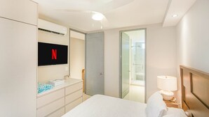 Una camera d'albergo con un letto, una TV a parete, un armadio, un comodino con una lampada e un box doccia in vetro.