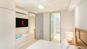 Ein Hotelzimmer mit einem Bett, einem an der Wand befestigten Fernseher, einem Kleiderschrank, einem Nachttisch mit Lampe und einer Duschkabine aus Glas.