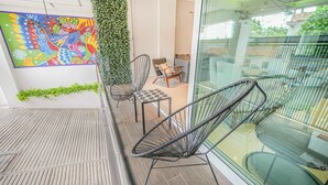 Un balcone moderno con ringhiera in vetro, un quadro astratto dai colori vivaci e un'area salotto con sedie.