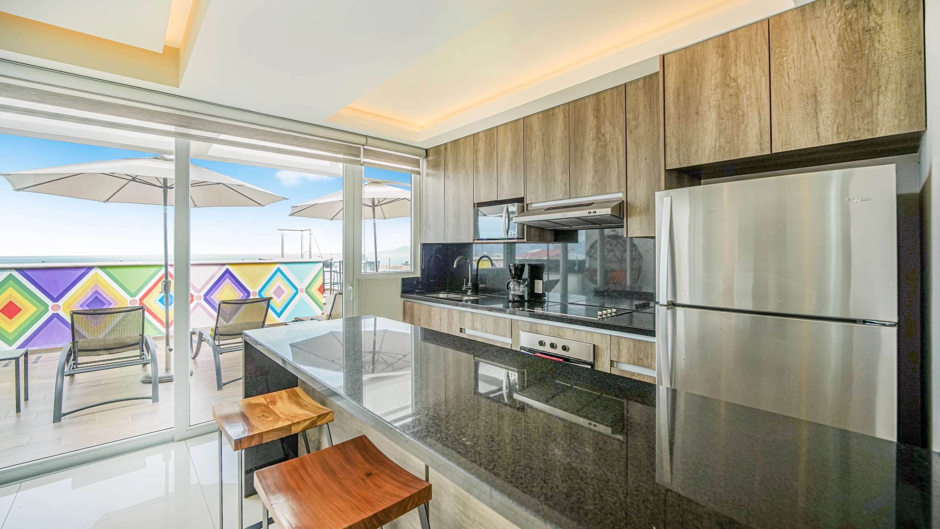 A modern kitchen with a stainless steel refrigerator, a microwave, and a coffee maker. There are wooden cabinets and a glass countertop.