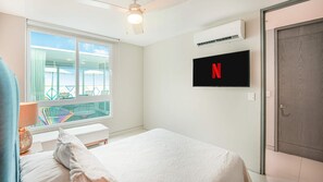 A bedroom with a bed, a TV mounted on the wall, and a window overlooking a balcony. - Torre Ku · Rooftop Pool with Ocean Views (Puerto Vallarta)
