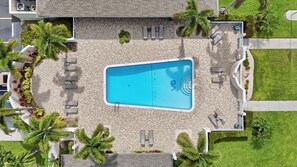 A rectangular swimming pool with a tiled deck, surrounded by lounge chairs and palm trees. - Close to Beach, Shops, Downtown - Great for Snowbirds (Naples)