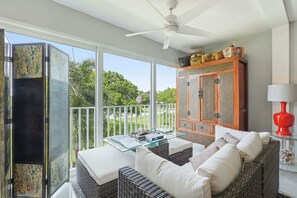 A balcony with wicker furniture, a glass table, and a view of greenery. - Close to Beach, Shops, Downtown - Great for Snowbirds (Naples)