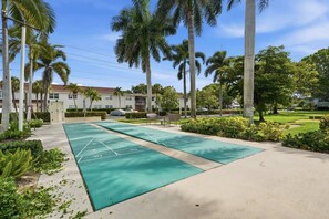 A courtyard with shuffleboard tables, palm trees, and a building in the background. - Close to Beach, Shops, Downtown - Great for Snowbirds (Naples)