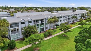 A multi-story building with a flat roof, surrounded by well-maintained lawns and trees. - Close to Beach, Shops, Downtown - Great for Snowbirds (Naples)