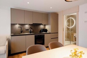 A modern kitchen with built-in appliances, a dining area with a table, and a glass-enclosed shower area. - Apartment Garnera 24 (Gaschurn)