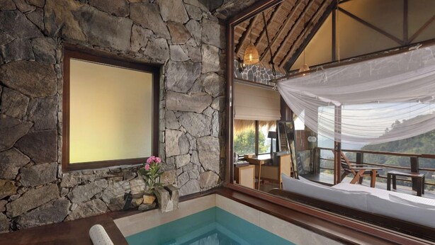 Ein Zimmer mit Steinwänden, einem Pool, einem großen Fenster und Blick auf einen Balkon.