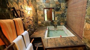 Ein Zimmer mit Steinwänden, einer Holzbänkl und einer Badewanne, mit einem kleinen Fenster.