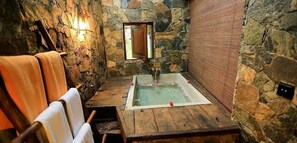 A stone-walled room with a wooden bench, a bathtub, and a small window. - 98 Acres Resort and Spa (Ella)
