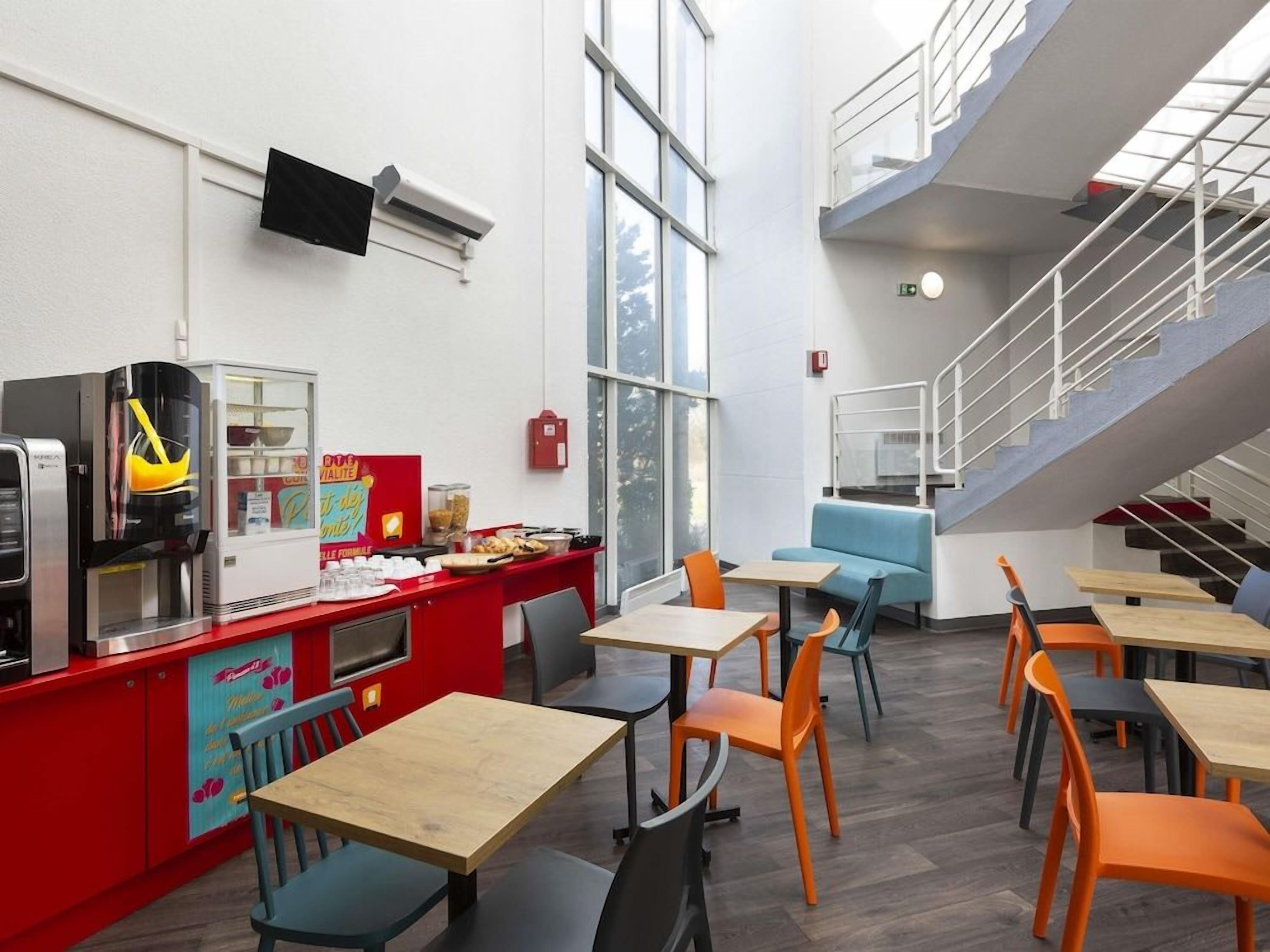 A modern indoor dining area with high ceilings, a staircase, and a counter with food items.