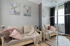 A modern living room with a sofa, cushions, a mirror, and artwork on the wall. - Cosy Apartment for 4 People | Workspace (Gdynia)