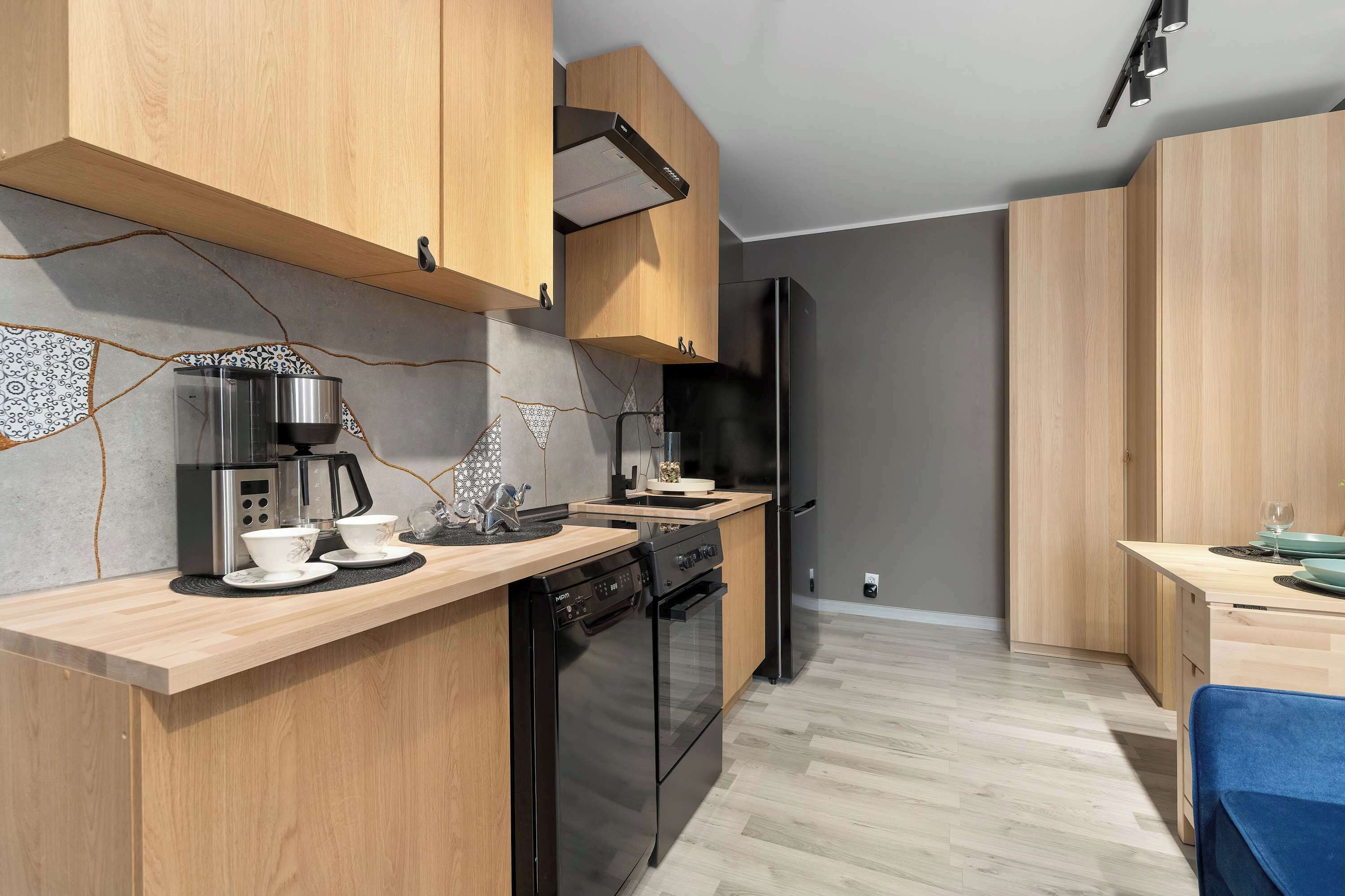 A modern kitchen with wooden cabinets, a built-in oven, a dishwasher, and a black refrigerator.