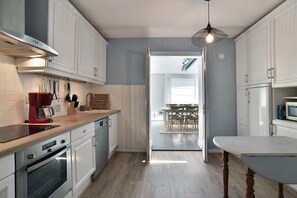 Une cuisine moderne avec des meubles blancs, un plan de travail en bois et un coin repas comprenant une table et des chaises.
