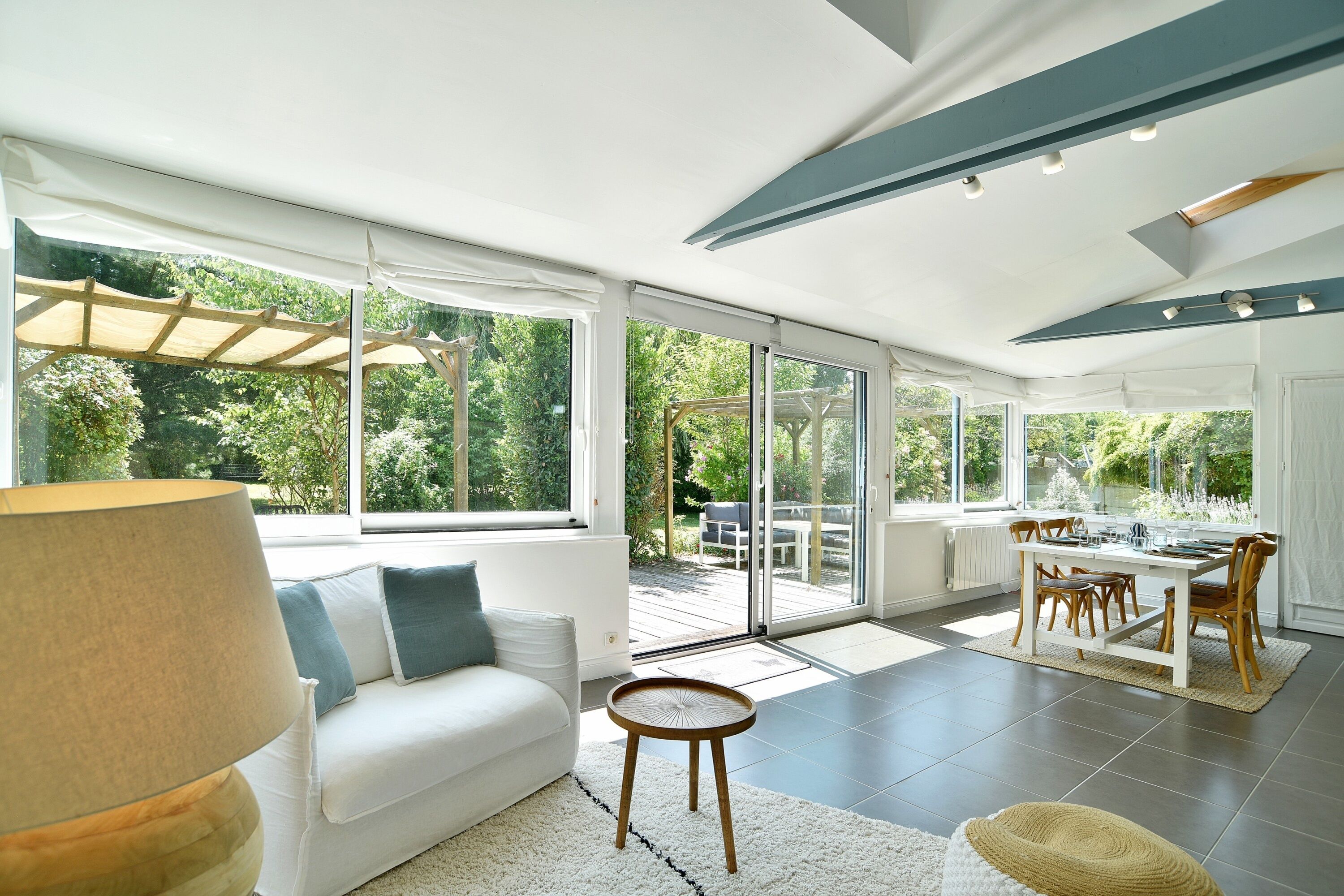 A spacious living area with a white sofa, a round wooden side table, and a view of a garden through large sliding glass doors.