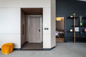 Un interior moderno con una puerta de madera, un otomano amarillo y una pared oscura con estanterías.