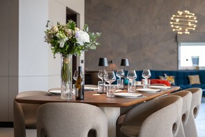 A dining table set with plates, glasses, and a bottle, surrounded by upholstered chairs. - Penthouse Annecy74 - Vue panoramique sur le lac (Annecy)