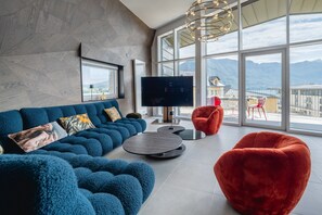 A modern living room with a large window, a sofa, a red chair, and a flat-screen TV. - Penthouse Annecy74 - Vue panoramique sur le lac (Annecy)